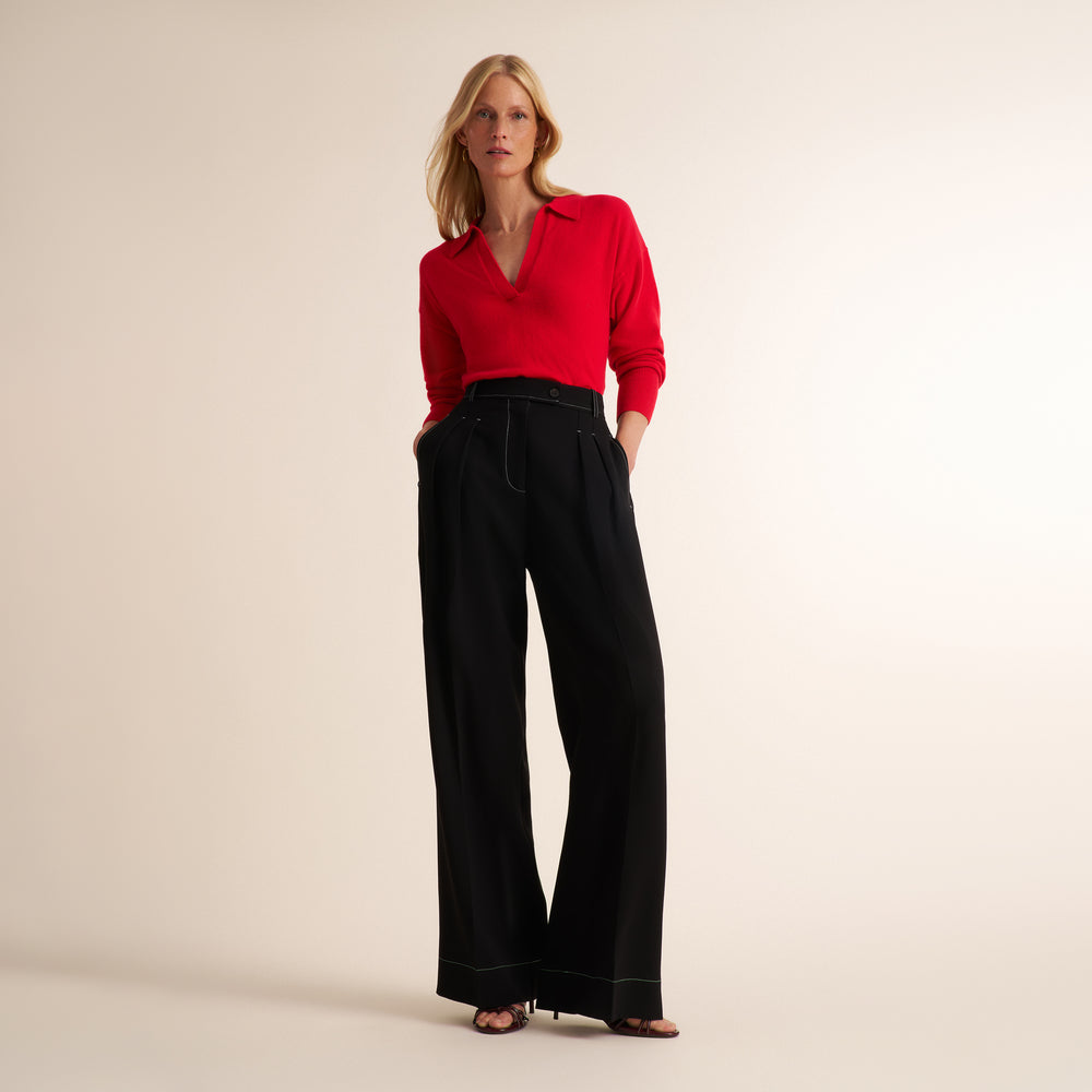 A woman modeling a bright red long-sleeve collared top paired with high-waisted black wide-leg trousers, standing against a plain beige studio background.