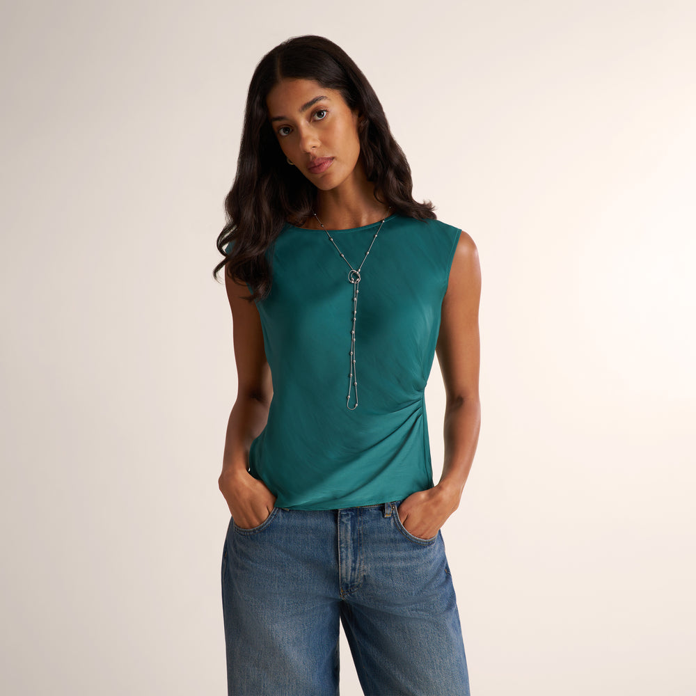 Woman wearing a peacock colored draped tank top and silver long necklace