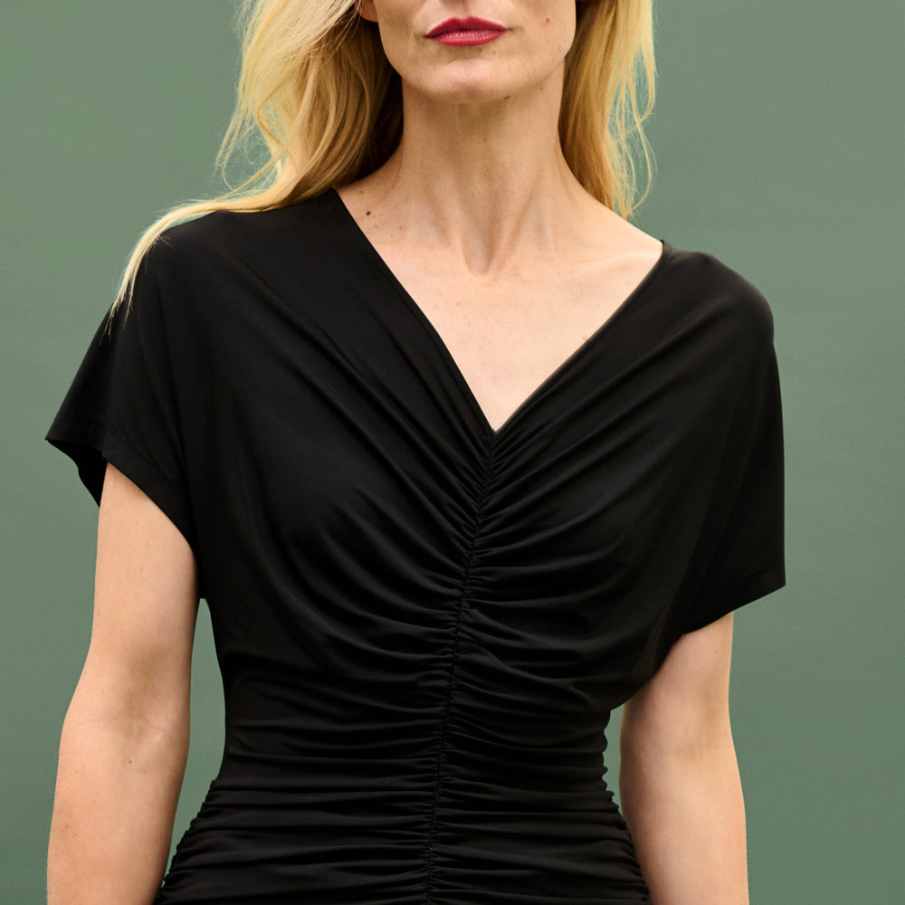Woman wearing a black dress with a draped neckline against a green background