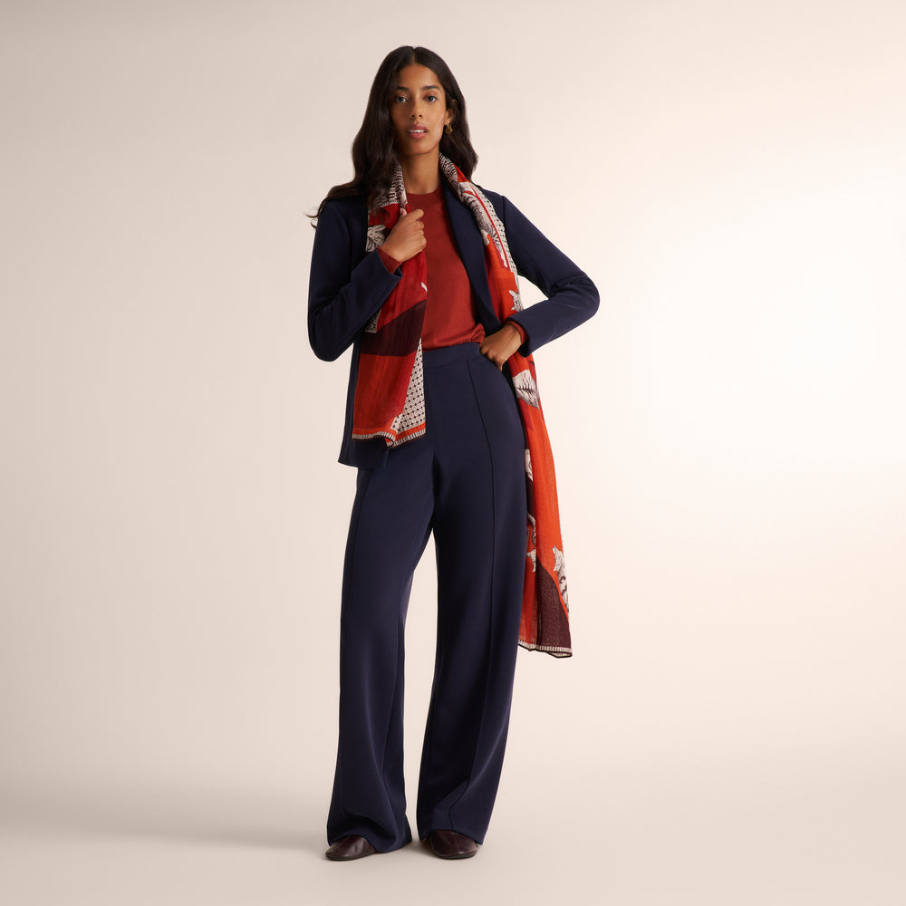 Woman wearing a orange spice color long sleeve sweater with a matching navy suit and orange and navy scarf around her neck