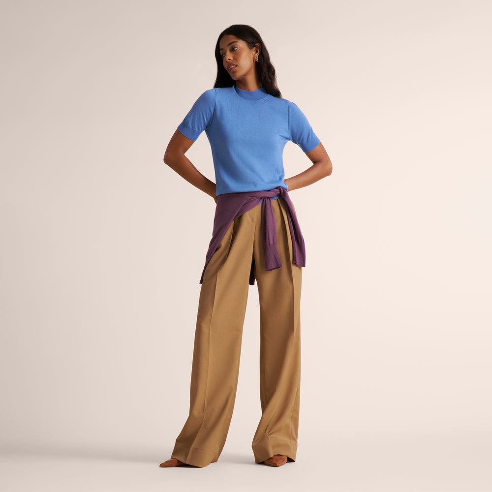 Woman wearing a blue splendor color short sleeve sweater with beige wide leg pants and a purple sweater tied around her waist