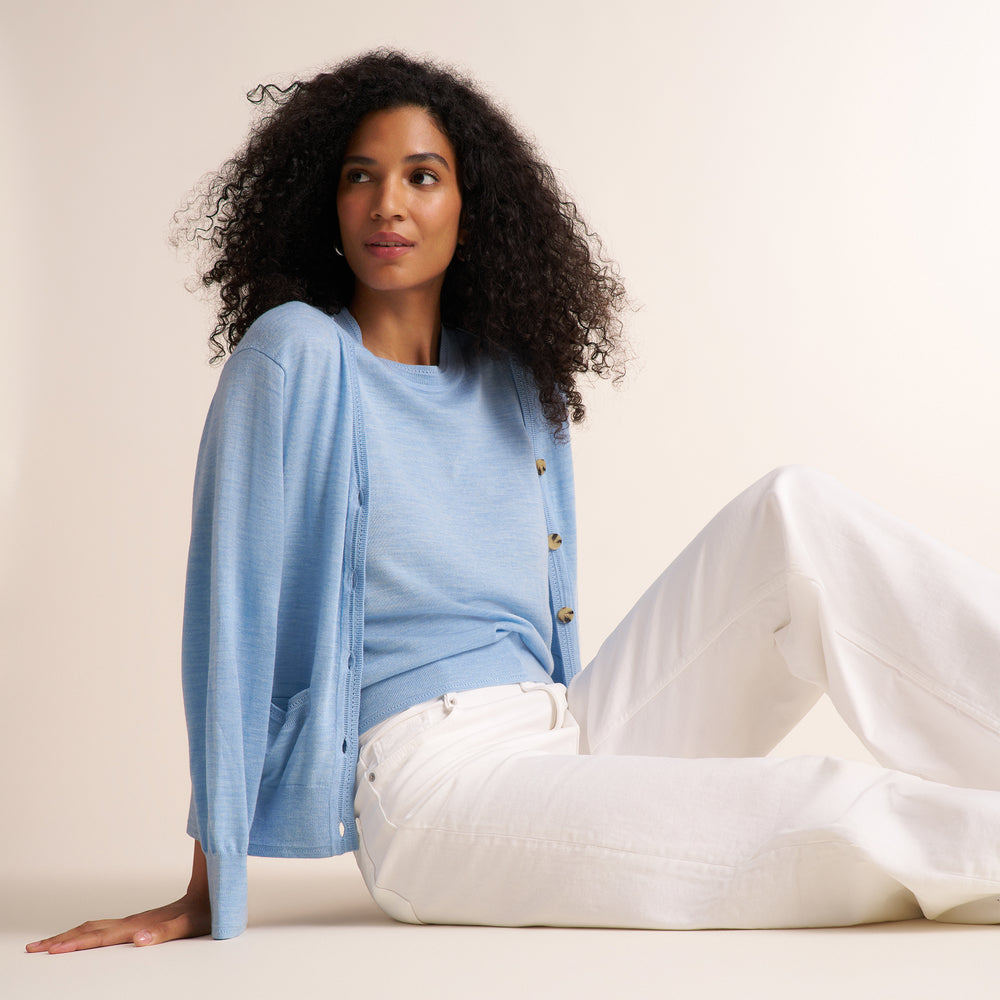Woman wearing alight blue short sleeve sweater tank with a matching cardigan and wide leg white jeans