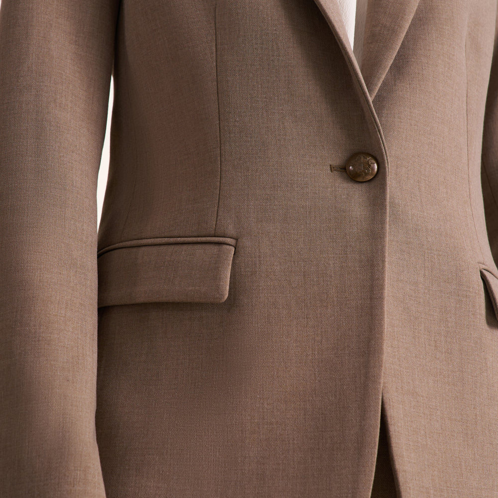 Close-up of a taupe brown blazer with a single button closure, showing the fabric texture and a white shirt underneath.