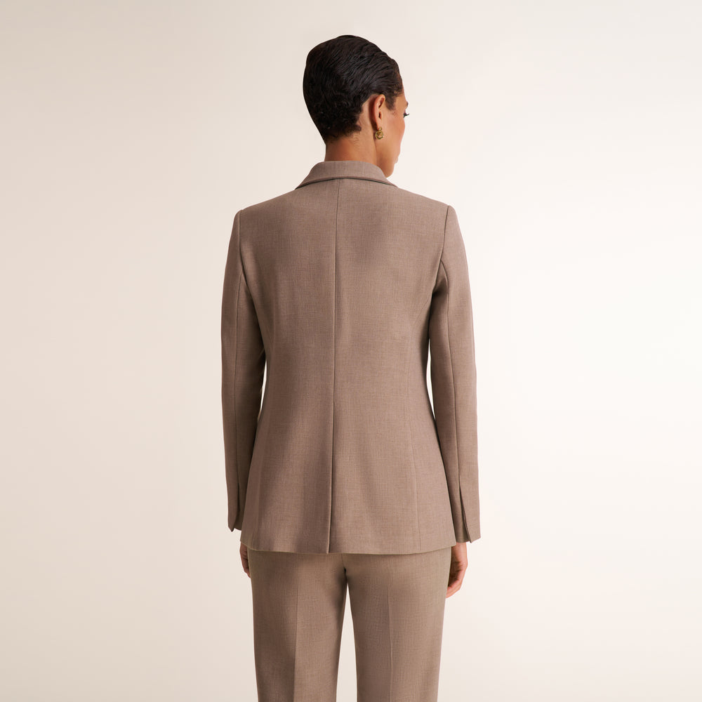 A model shown from the back wearing a taupe brown tailored blazer and matching trousers against a plain light beige studio background.