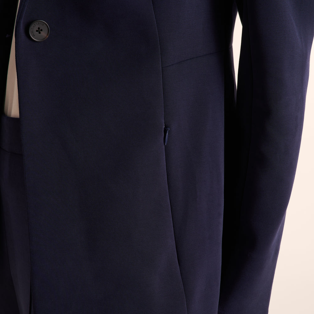 Close-up of a dark navy blue suit jacket, showing a buttoned lapel, a side pocket, and the fabric texture against a light background.