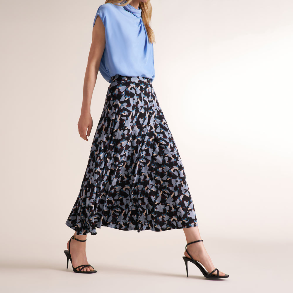 Woman wearing a light blue sleeveless top and a printed skirt on a beige background