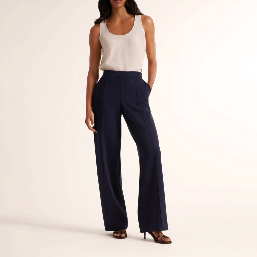 A model wearing navy blue wide-leg trousers and a cream sleeveless top, standing against a plain off-white studio background.