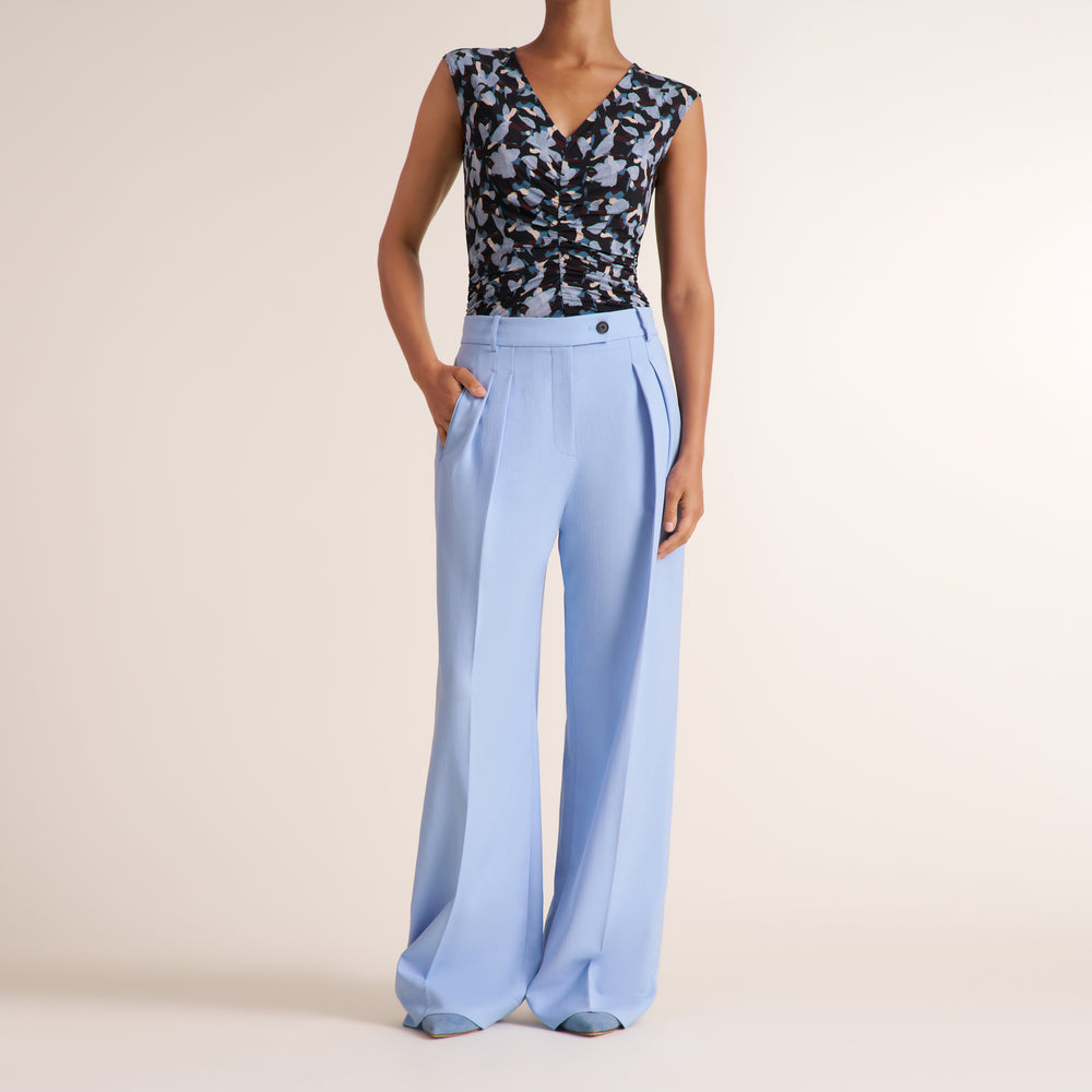 Woman wearing a light blue pant and floral top on a beige background