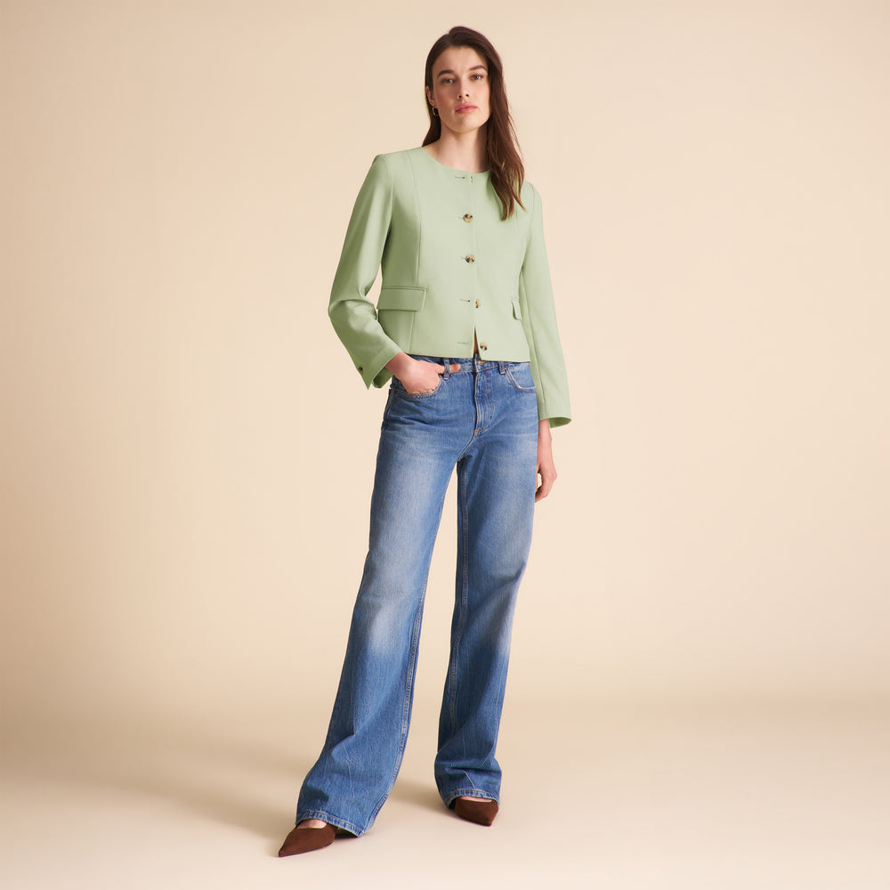 Woman wearing a light green jacket and blue jeans on a beige background