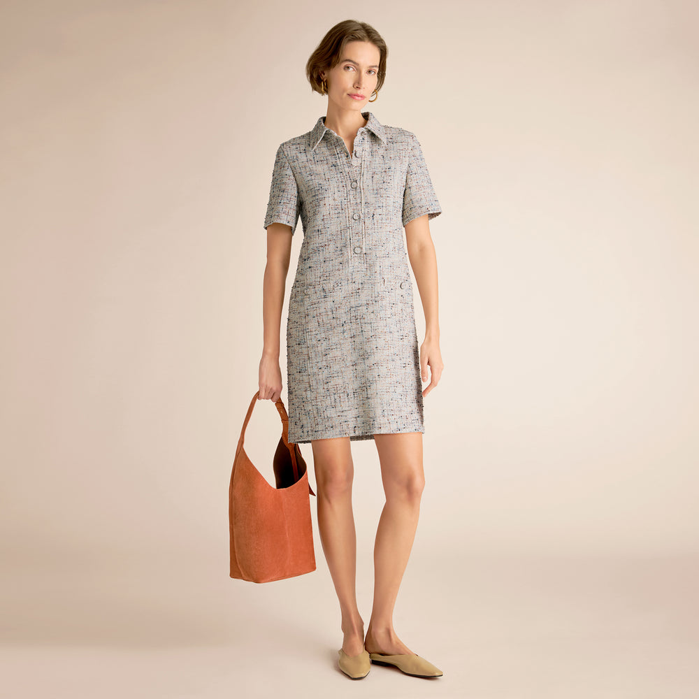 Woman wearing a checkered dress holding an orange bag on a beige background