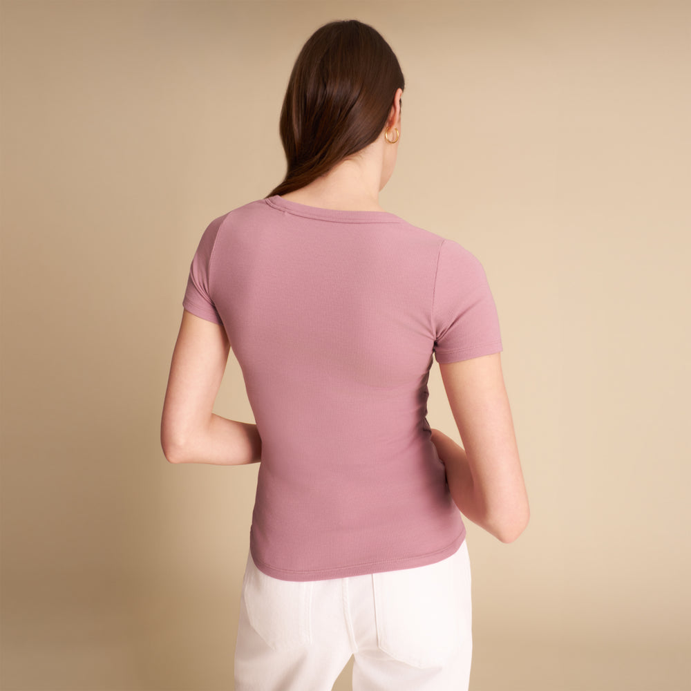 Woman wearing a mauve t-shirt and white pants on a beige background