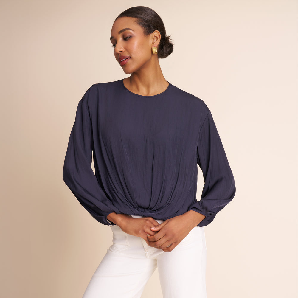 Woman wearing a dark blue long-sleeve top and white pants on a beige background