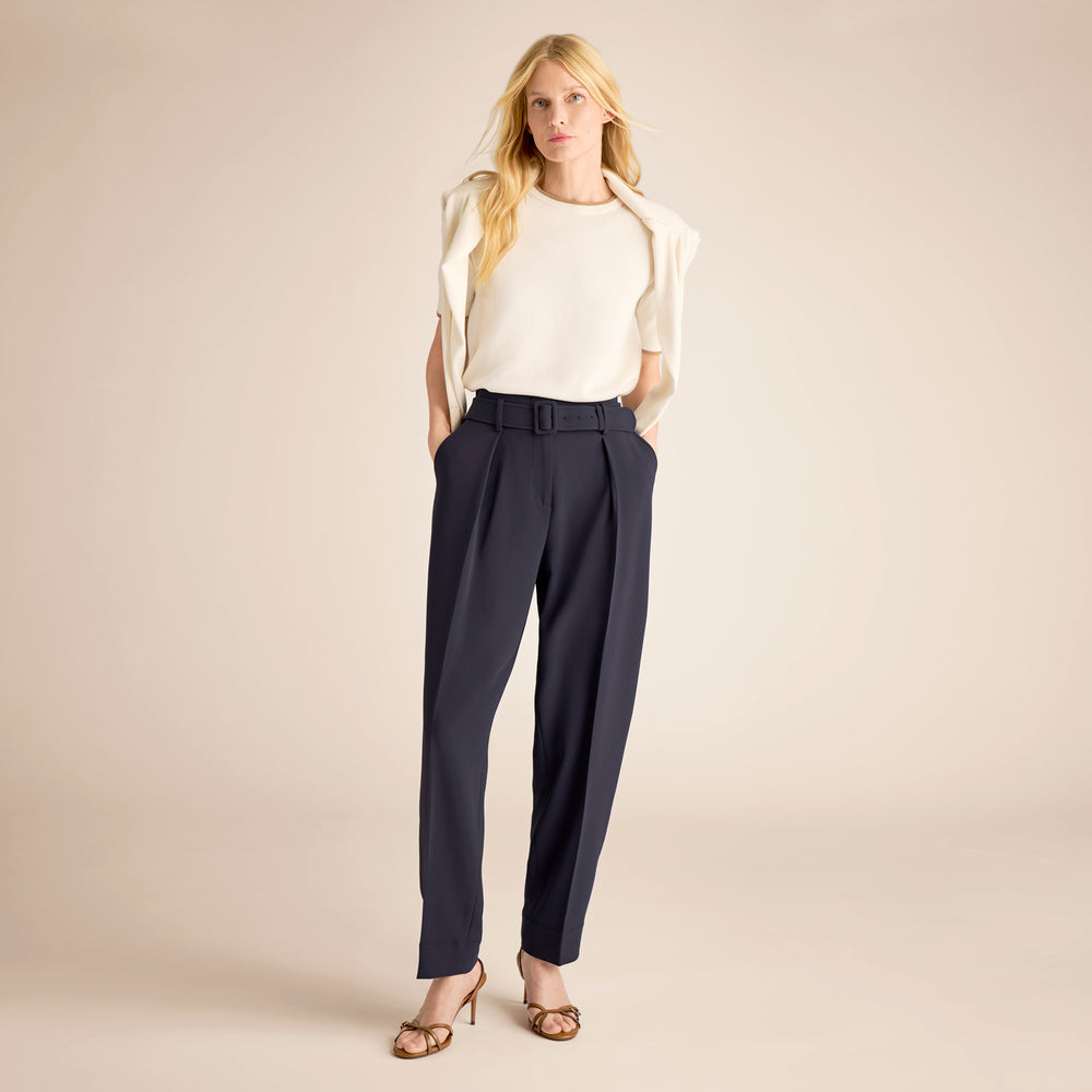 Woman wearing a white blouse and navy pants on a beige background