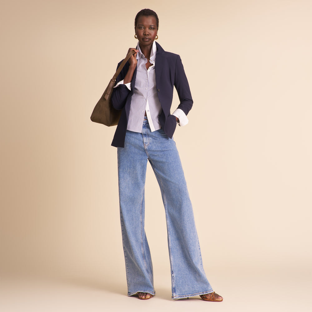Woman in navy blazer with matching pants and striped shirt sitting against a beige background