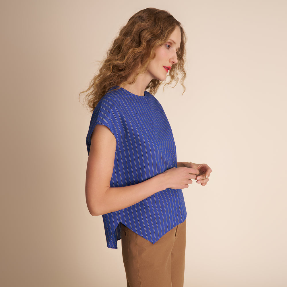Woman wearing a blue striped top and brown pants against a beige background