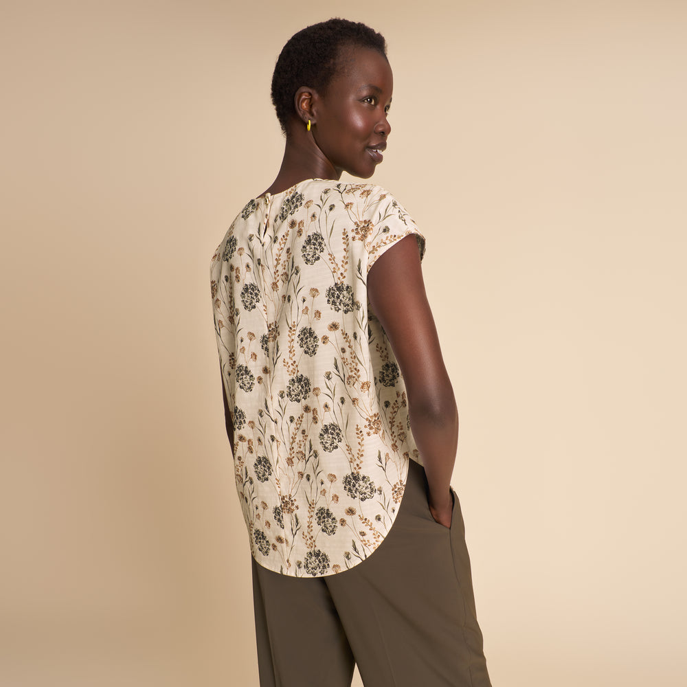 Woman wearing a floral blouse and brown pants against a beige background