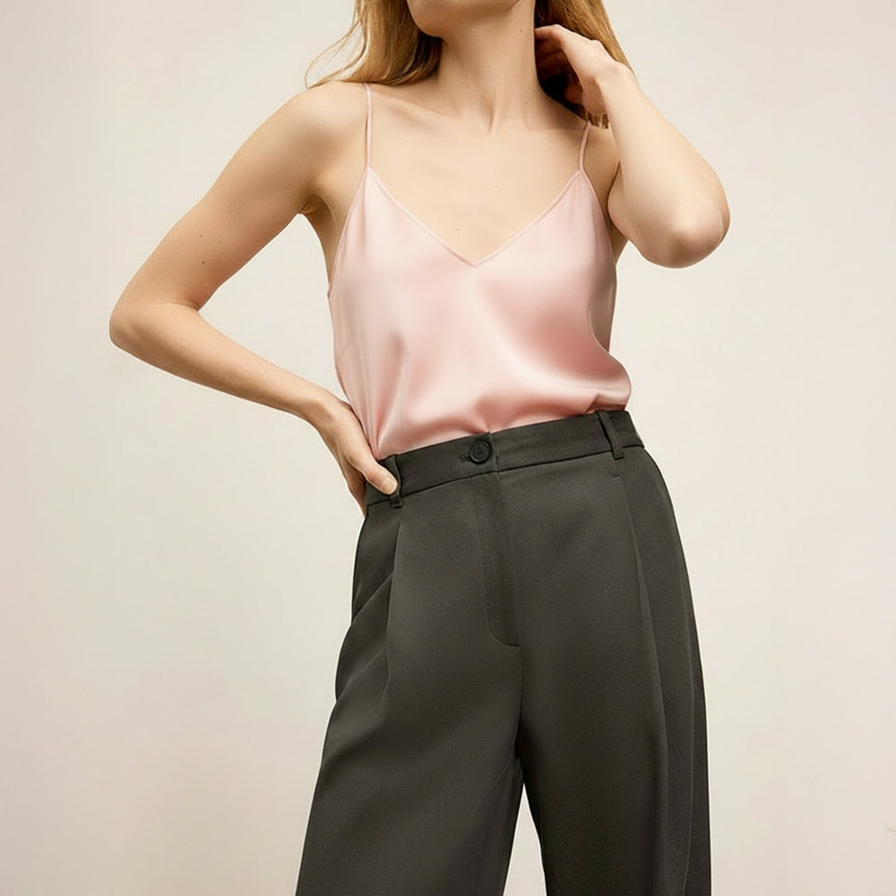 Woman wearing a pink satin top and dark gray pants on a beige background