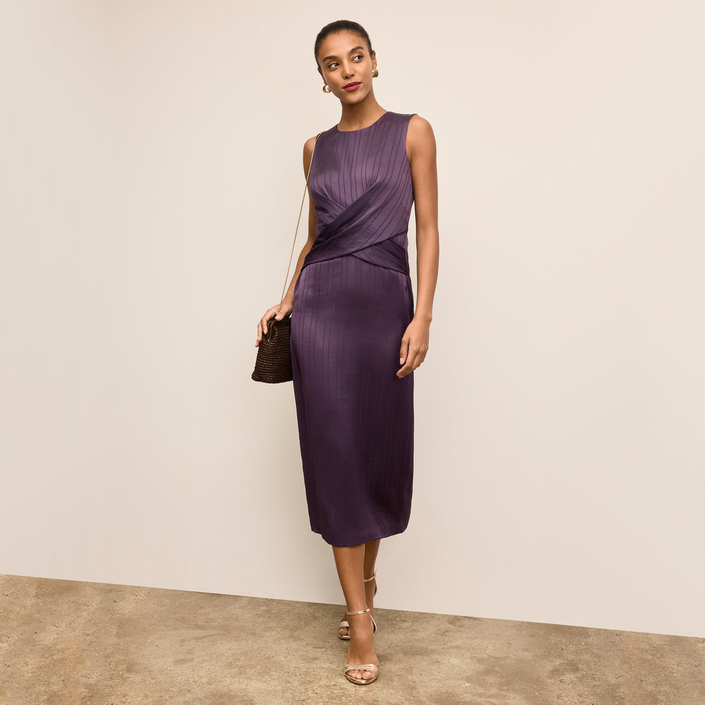 Woman wearing a purple dress holding a black handbag against a beige background