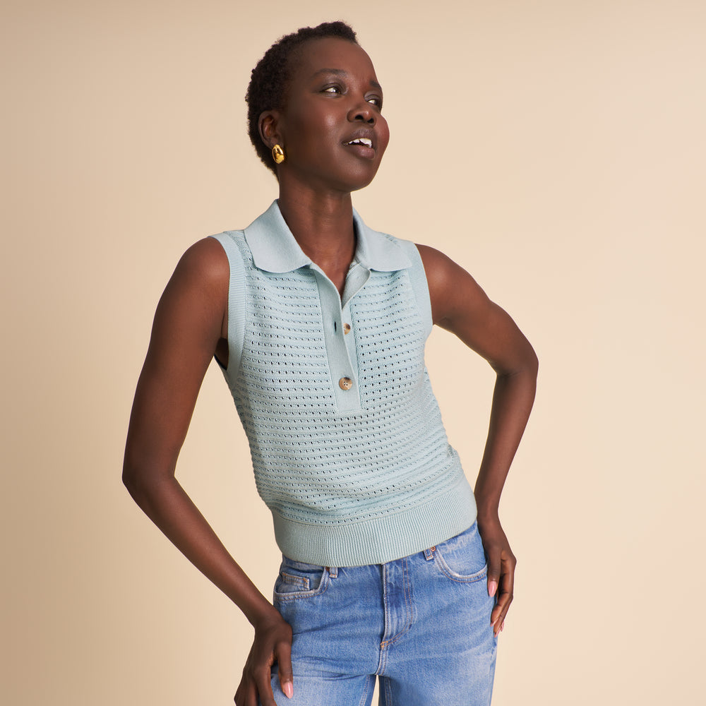 Woman wearing a light blue knitted top with black buttons on a beige background