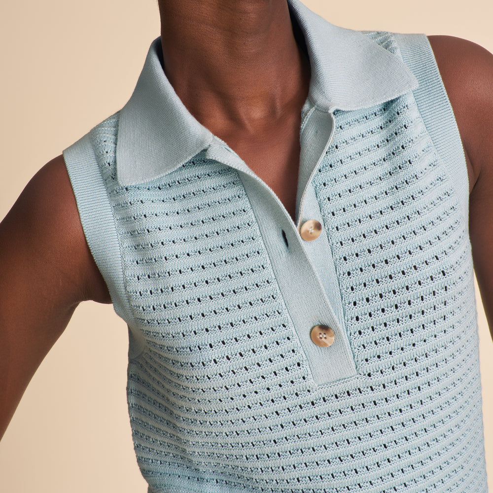 Woman wearing a light blue knitted top with black buttons on a beige background