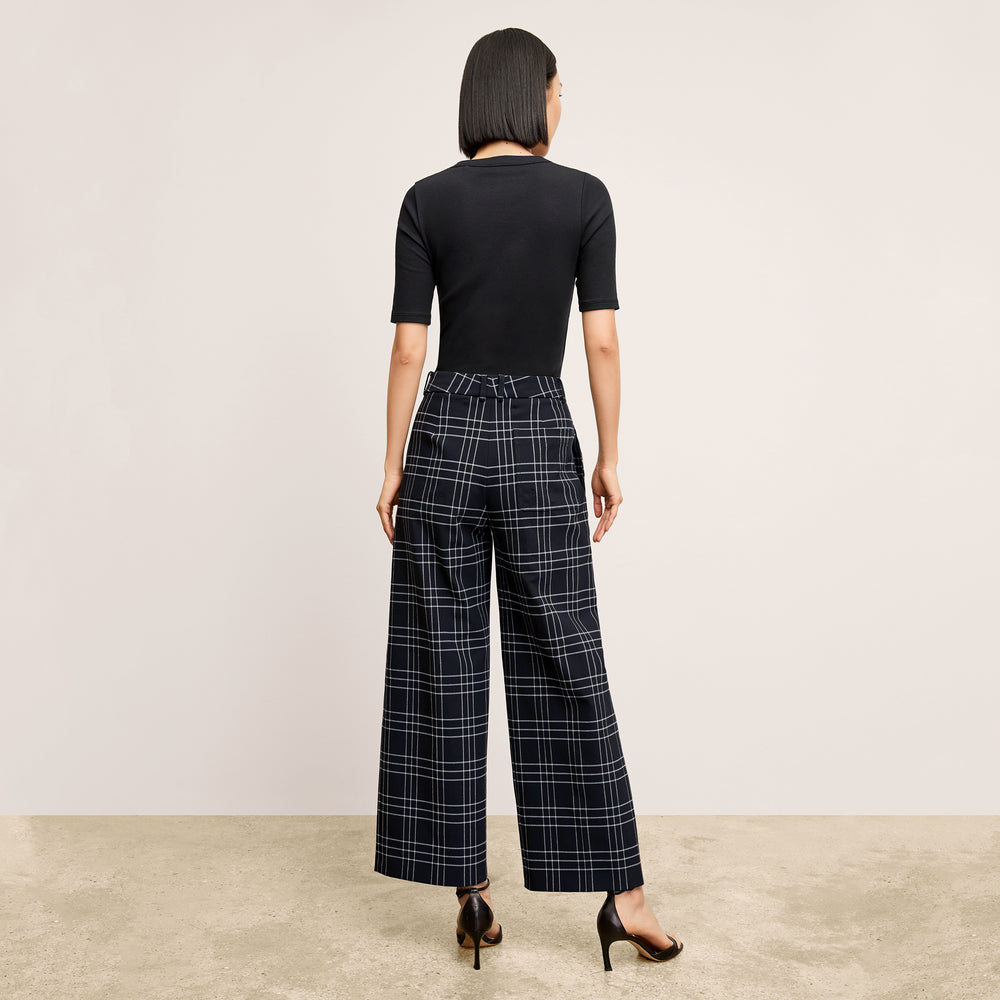 Woman wearing a black top and plaid pants on a plain background