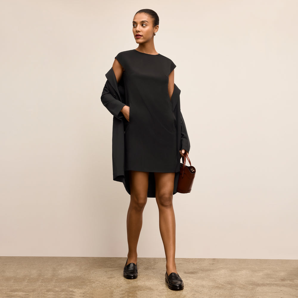 Woman wearing a black dress holding a brown leather bag against a beige background