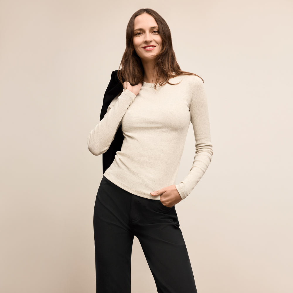 Woman wearing a beige sweater and black pants against a plain background Lead