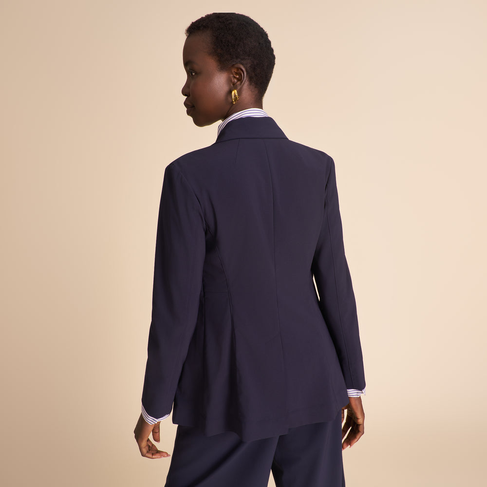 Woman in navy blazer with matching pants and striped shirt sitting against a beige background