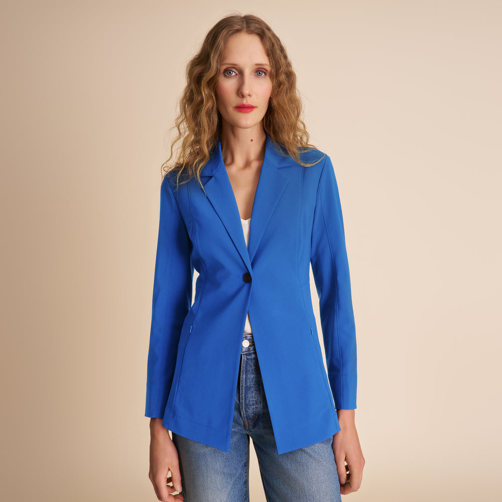 Woman wearing a blue blazer over a white top and jeans on a beige background