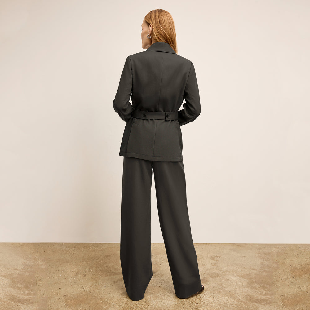 Woman wearing a dark gray suit standing against a plain background