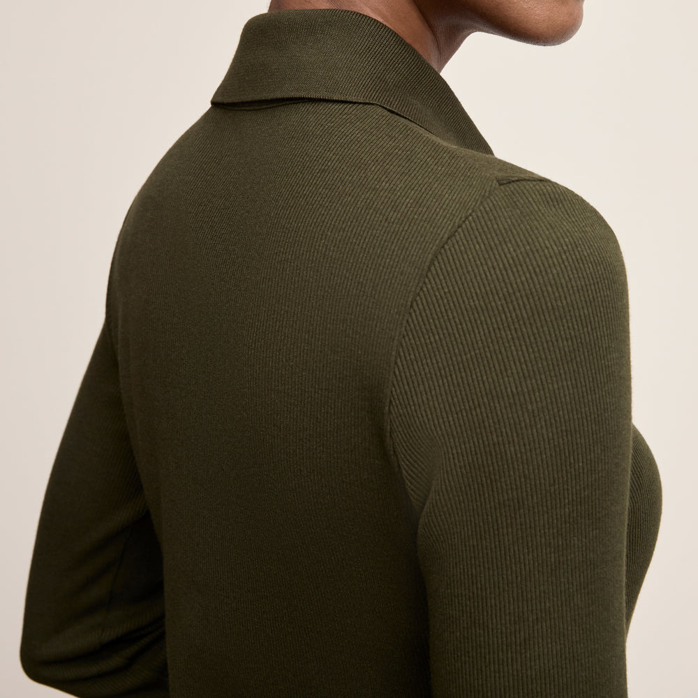 Person wearing a green ribbed sweater against a beige background