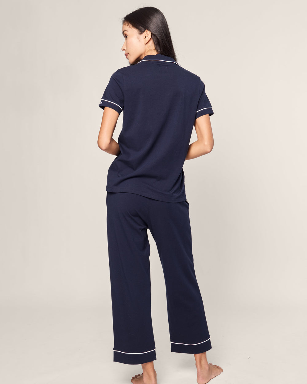 Person wearing navy blue pajama set with white trim on a light gray background