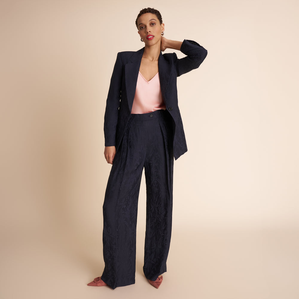 Woman wearing a navy suit with a pink top on a beige background