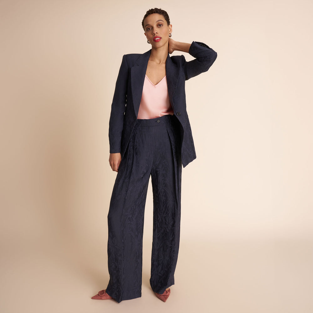 Woman wearing a navy suit with a pink top on a beige background