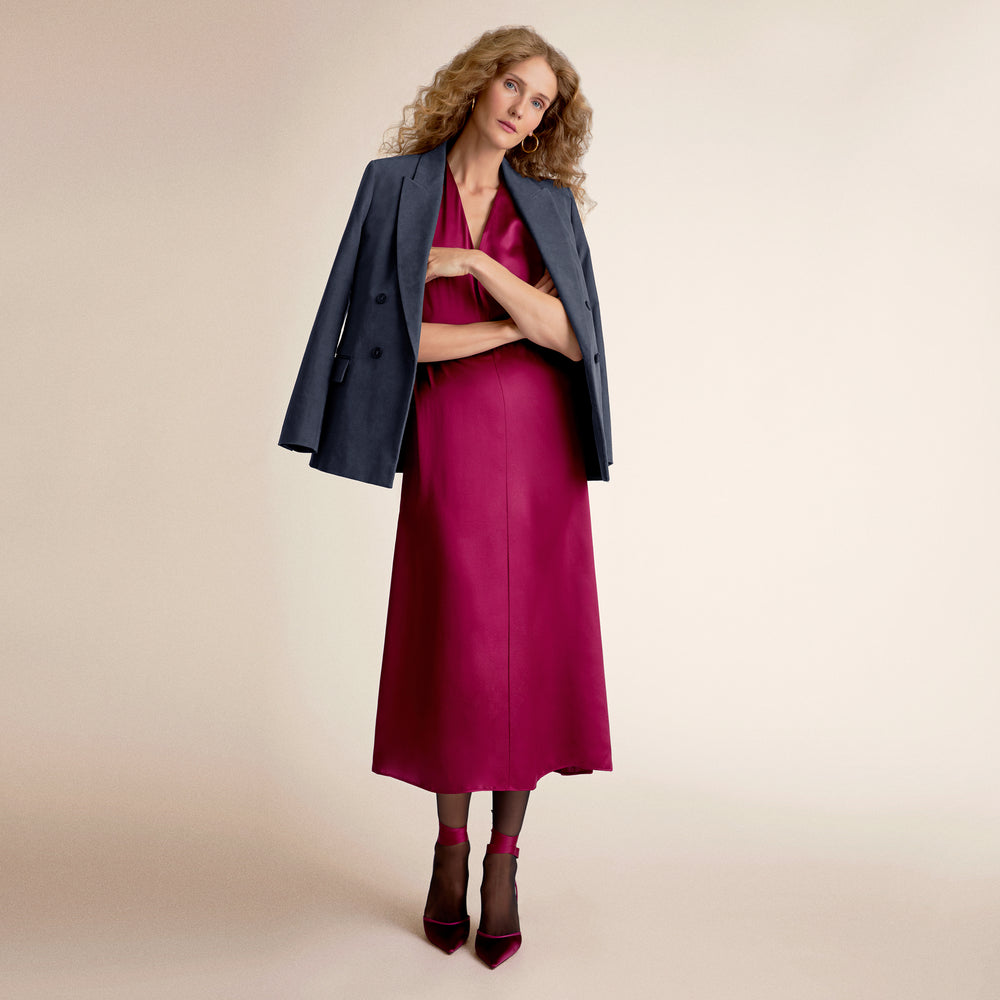 Woman wearing a dark blue blazer over a magenta dress on a beige background
