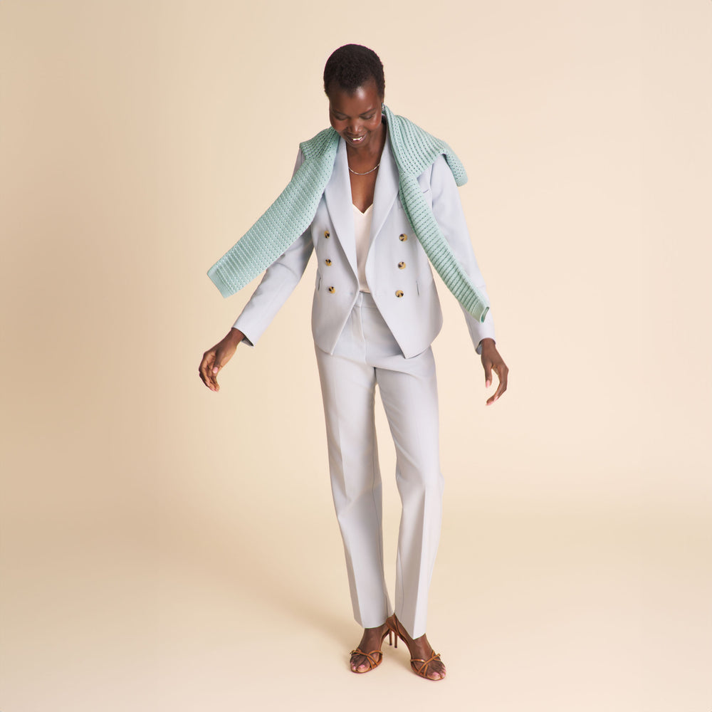Woman wearing a light blue blazer and matching pants on a beige background