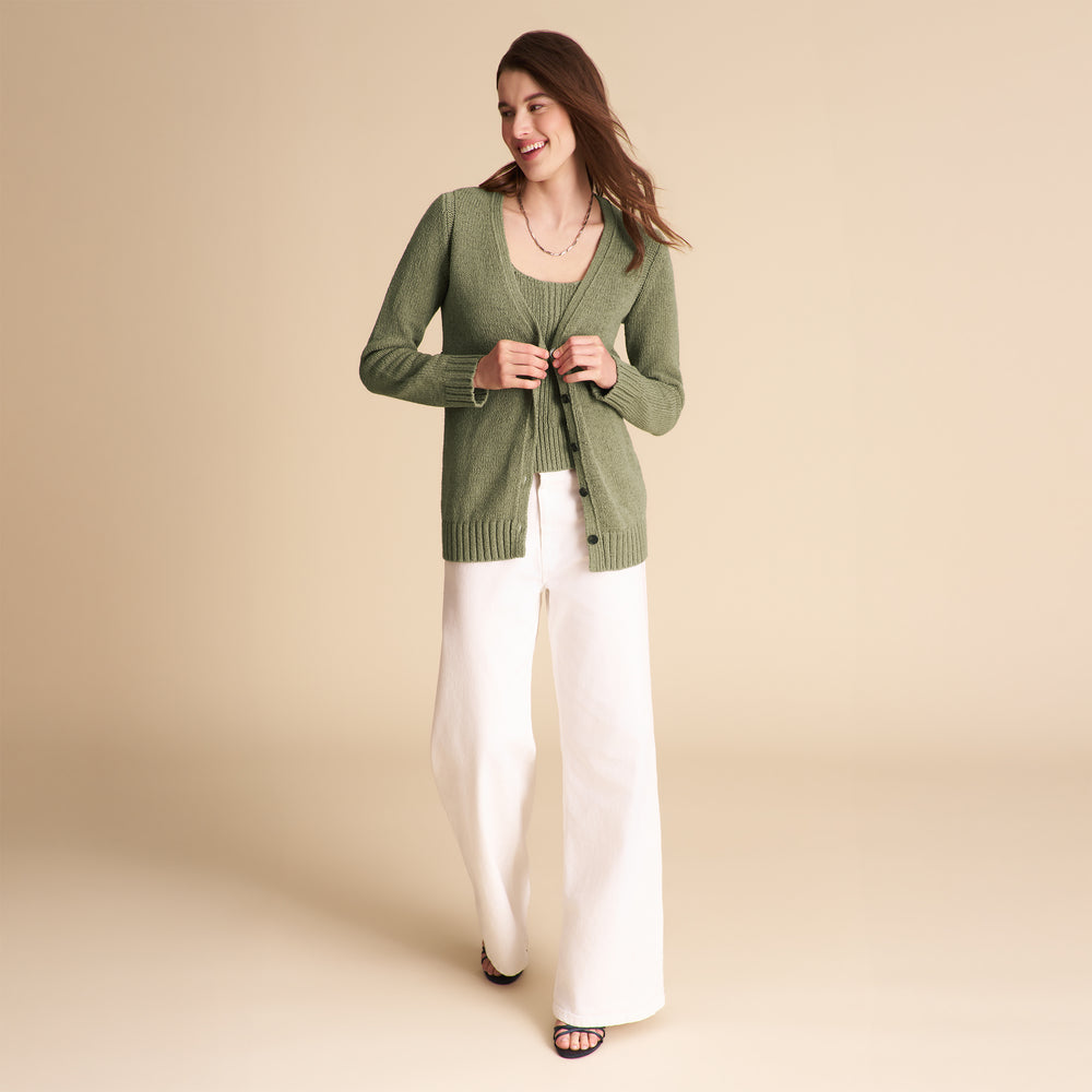 Woman wearing a green cardigan and white pants on a beige background
