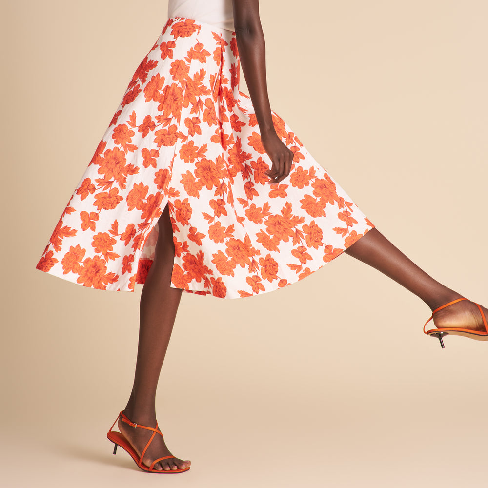 Woman wearing a white cardigan, floral skirt, and high-heeled shoes on a beige background