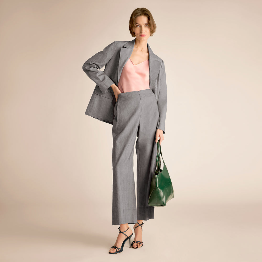 Woman wearing a gray suit holding a green bag on a beige background
