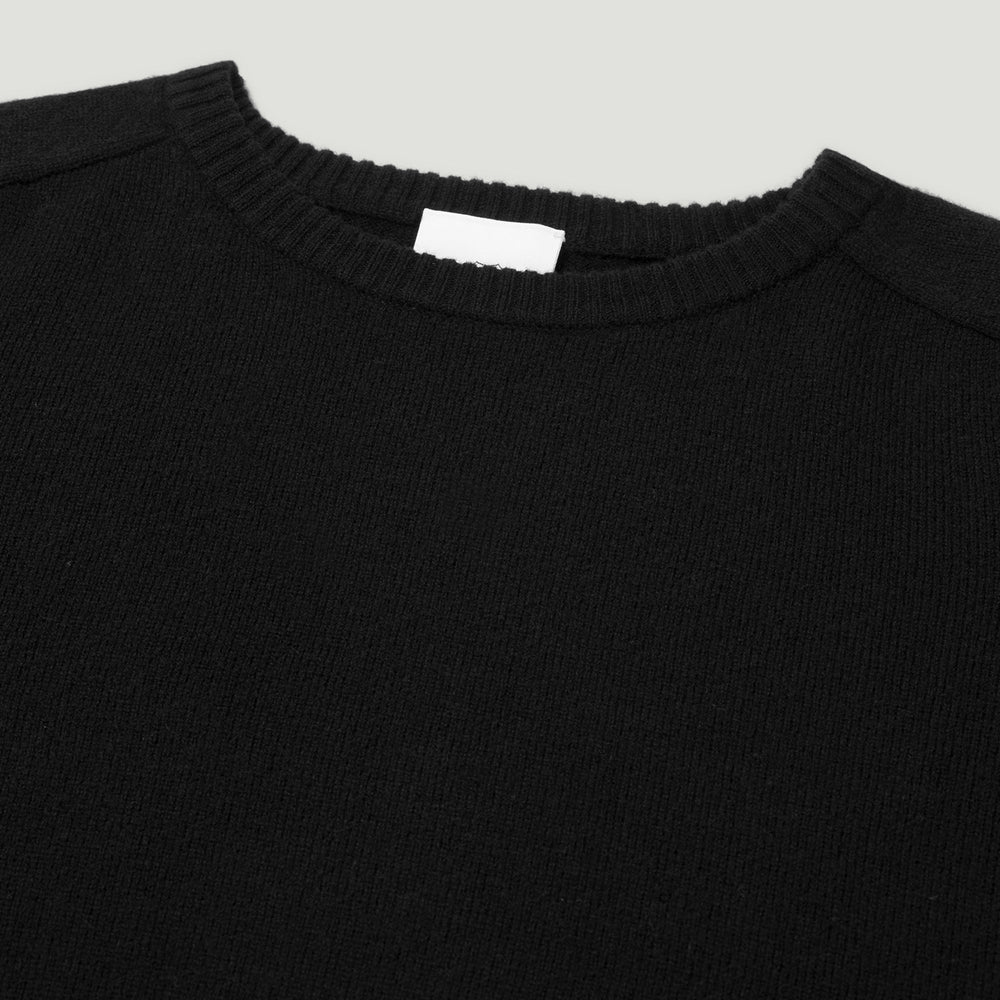 Close-up of a black sweater with a visible brand label on a light gray background