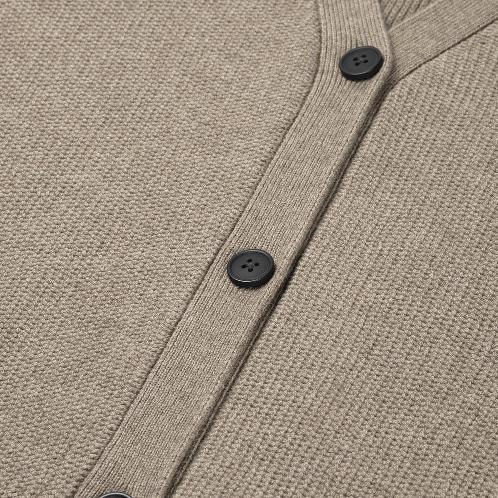 Close-up of a beige cardigan with black buttons on a matching fabric background