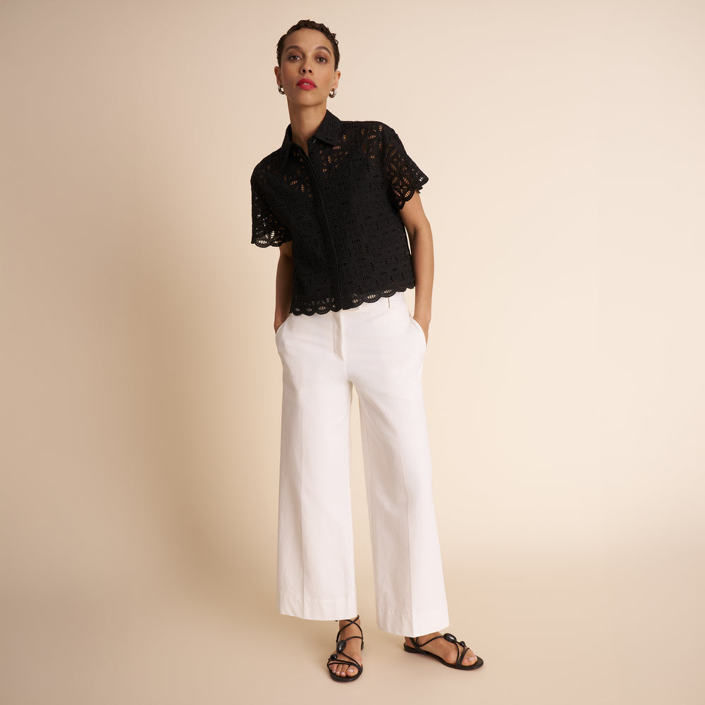 Woman wearing a black lace top and white pants on a beige background