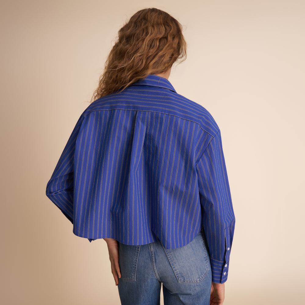 Person wearing a blue striped shirt and jeans on a beige background
