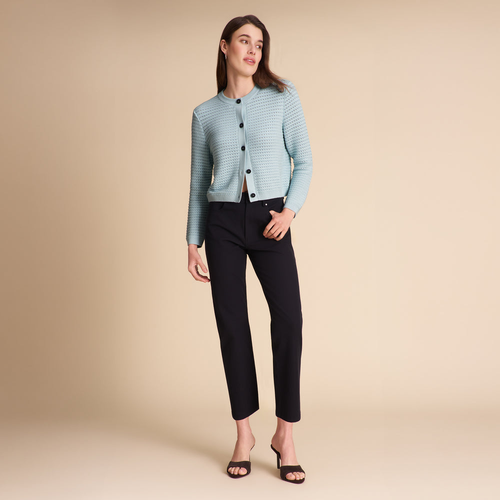 Woman wearing the Zosia cardigan in light blue on a beige background