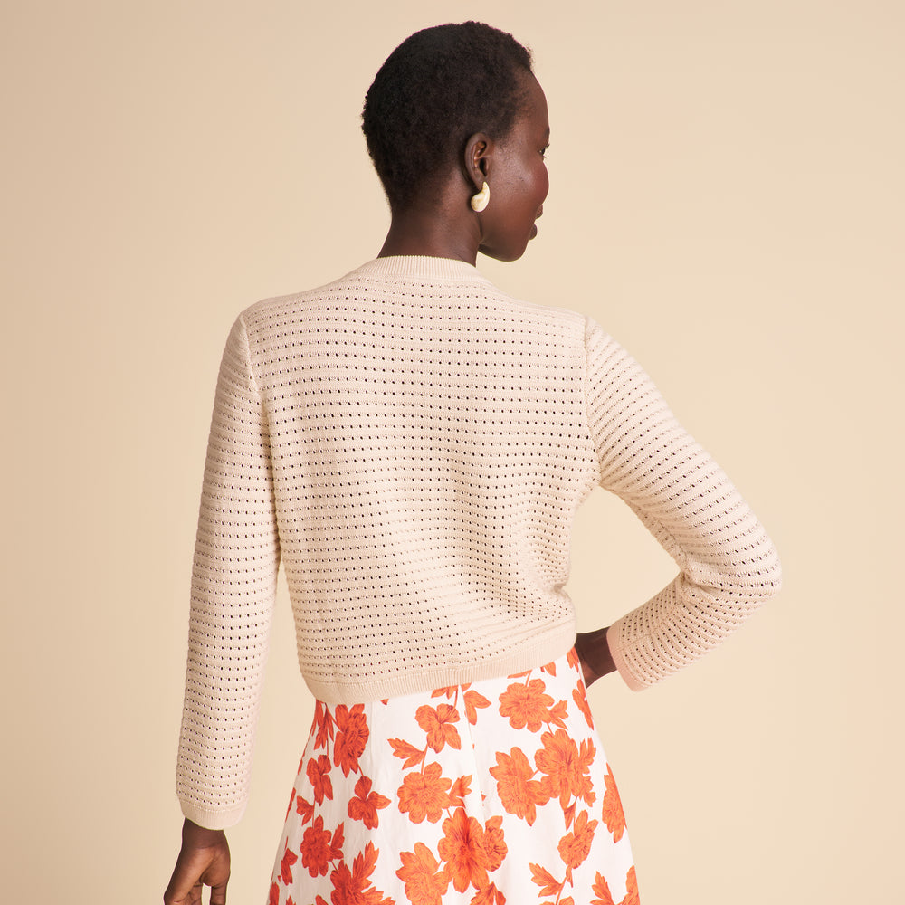 Woman wearing a beige crochet sweater and floral skirt on a beige background