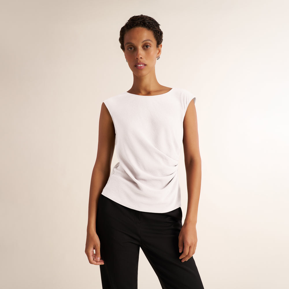 Woman wearing a white, draped cap sleeve shirt with black pants