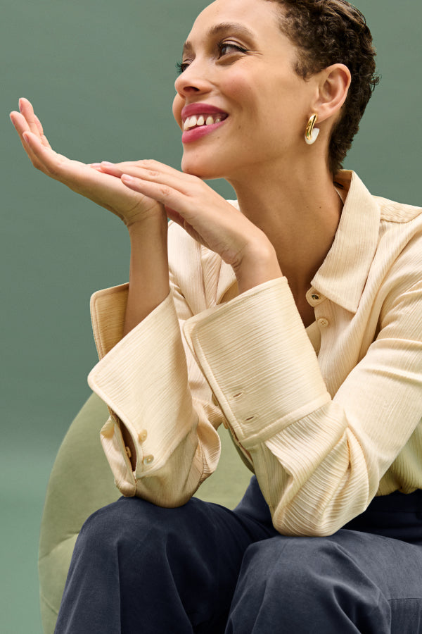 Woman in a beige jacket with hands near her face against a green background