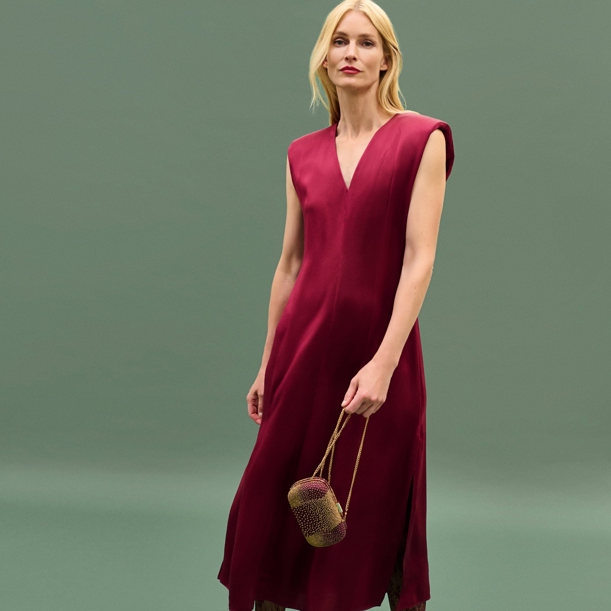 Woman wearing a burgundy dress holding a woven bag against a green background