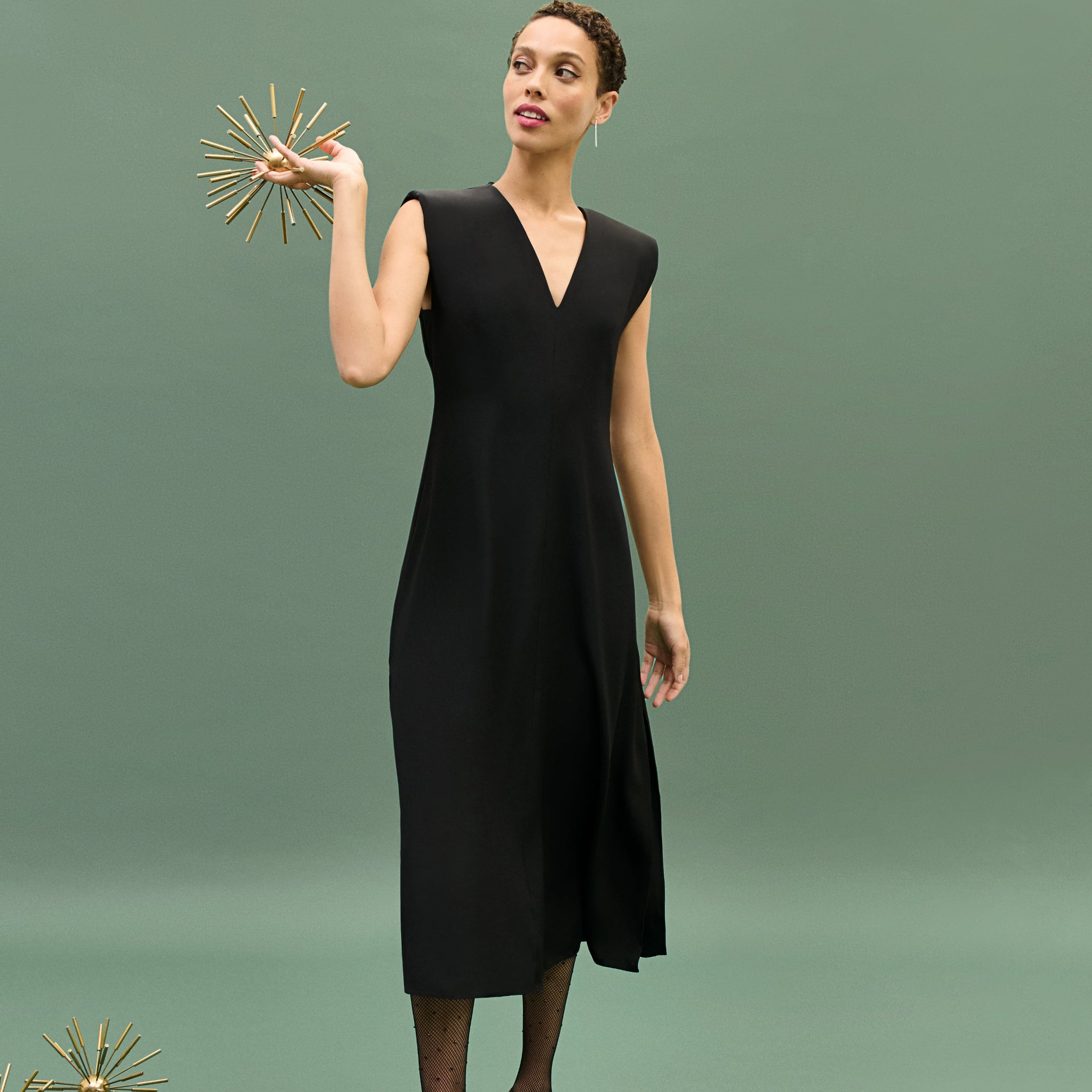 Woman in a black dress holding a decorative object against a green background