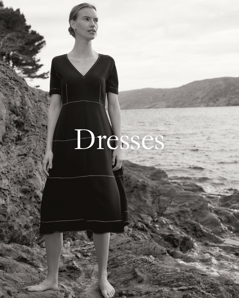 Woman in a black dress standing on a rocky beach with 'Dresses' text overlay.